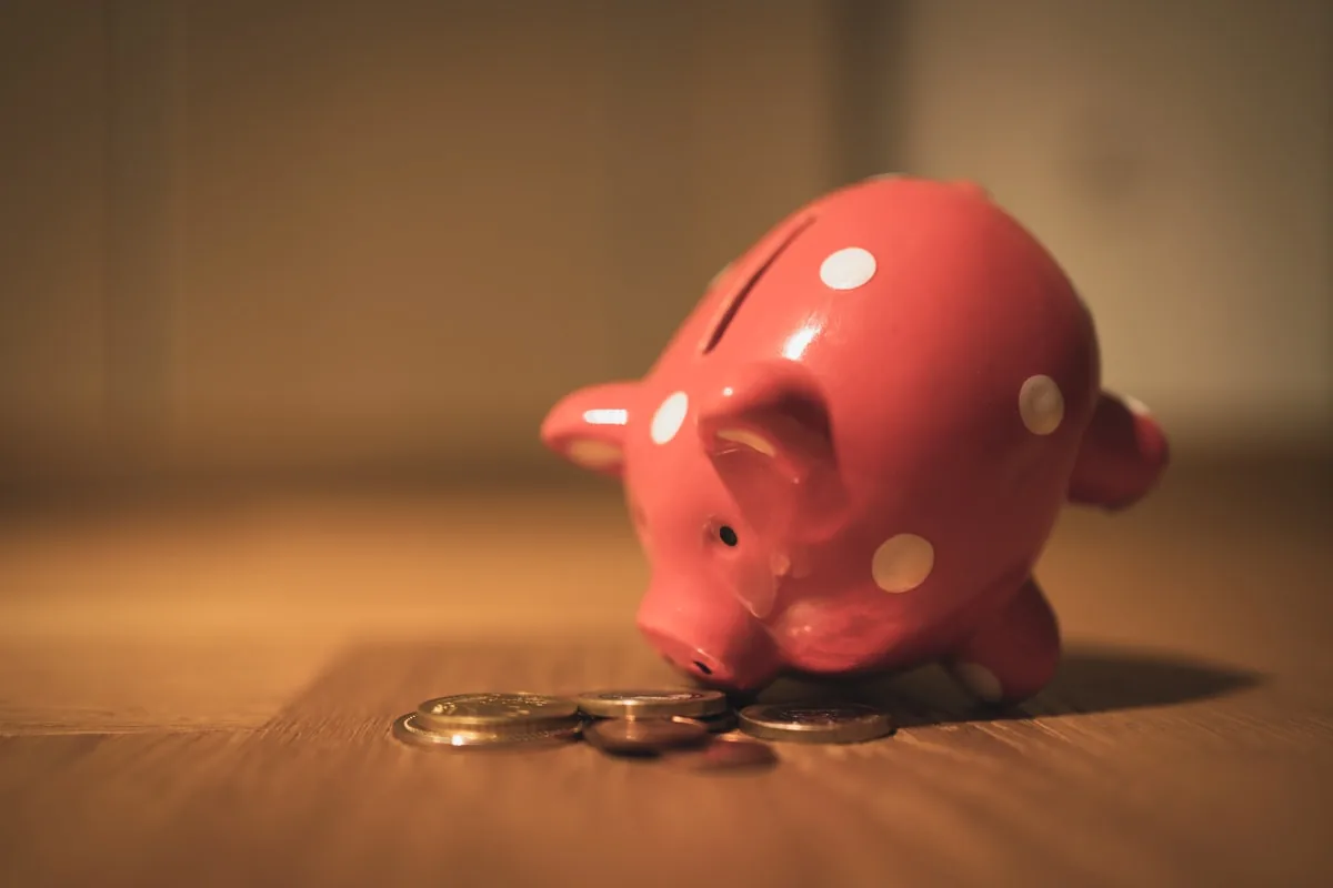 Cofrinho de porcelana rosa com moedas ao lado, representando a poupança